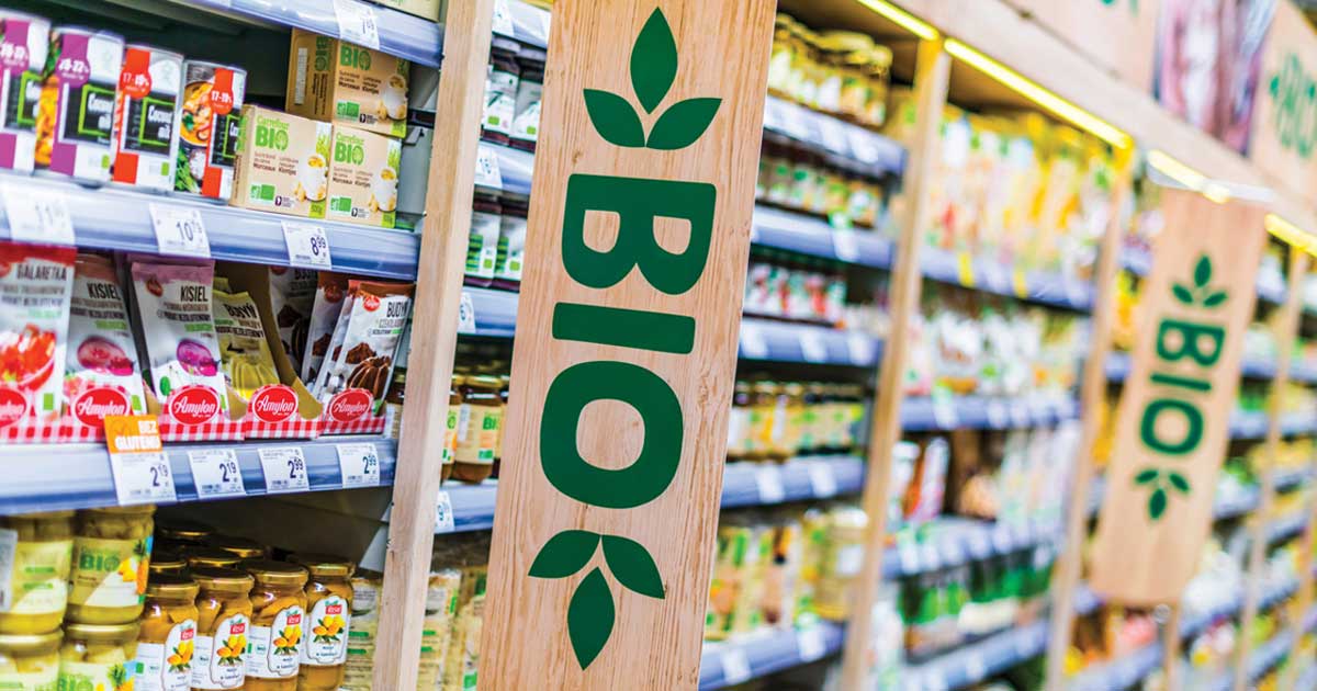 Raft de supermarket cu produse etichetate eco verde, consumator citind eticheta, România 2026, protecția consumatorilor