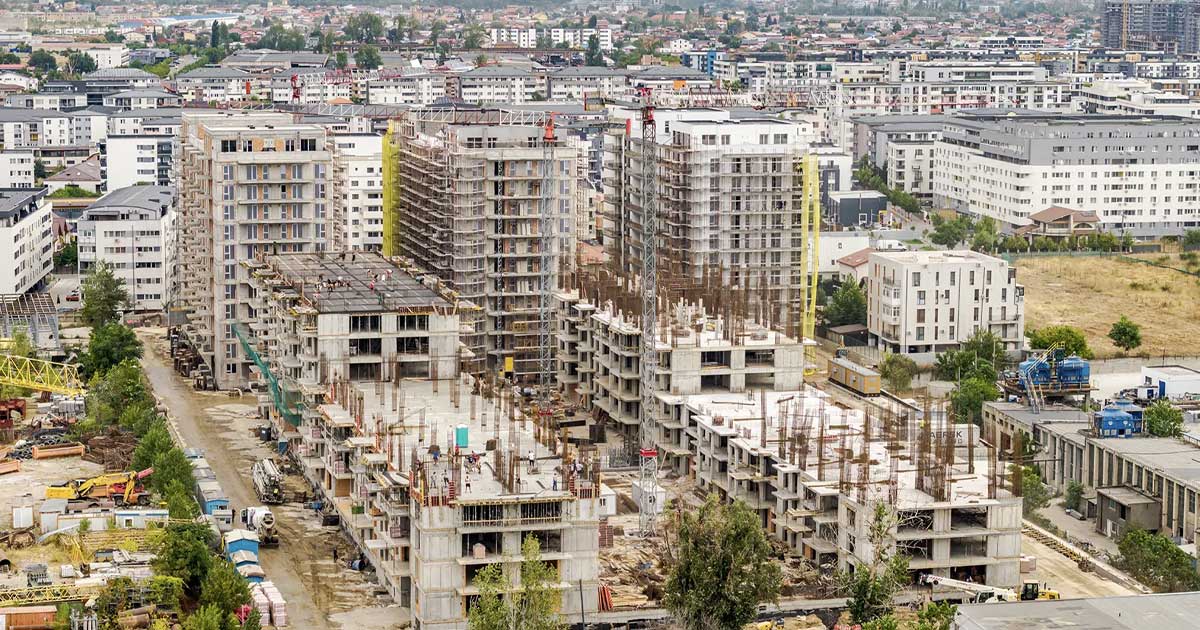 Ansamblu rezidențial nou în construcție la marginea unui oraș din România, macarale și blocuri neterminate, august 2026