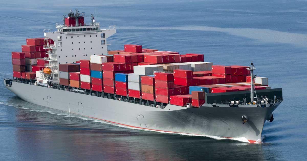 Navă de marfă în larg, cu containere pe punte și un petrolier în depărtare, sub cer înnorat